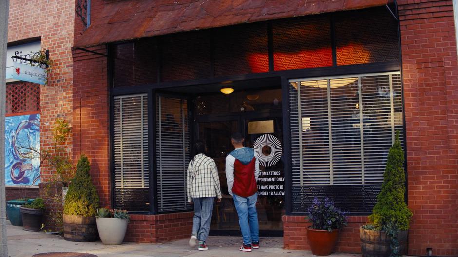 Naomi and Nathan approach Dee's tattoo shop.