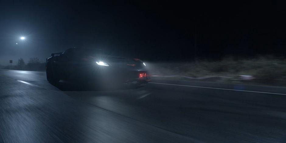 The Batmobile shoots out a grappling hook at a car while speeding down the road.