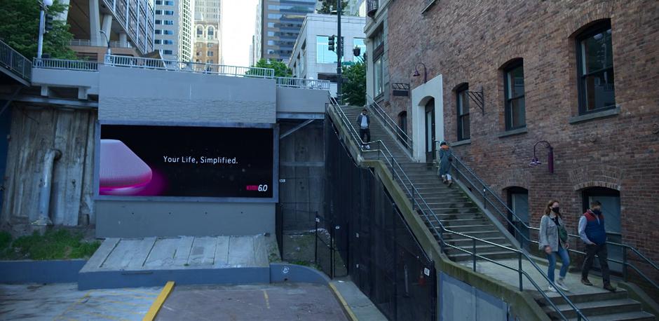 Angela walks up the stairs past an advertisement for Kimi 6.0.