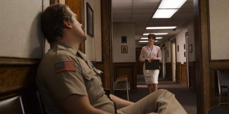 Hopper sits in the hallway waiting for his meeting with the mayor as the mayor's secretary Candice approaches to tell him the mayor is ready.