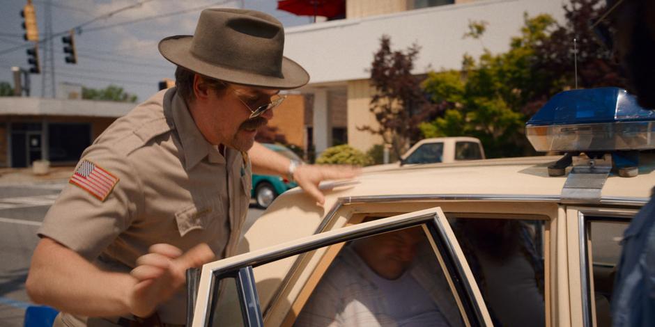 Hopper forces one of the protestors into the back of a police car.