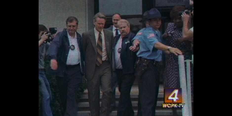 Mayor Kline is escorted out of the town hall in handcuffs on a news report.