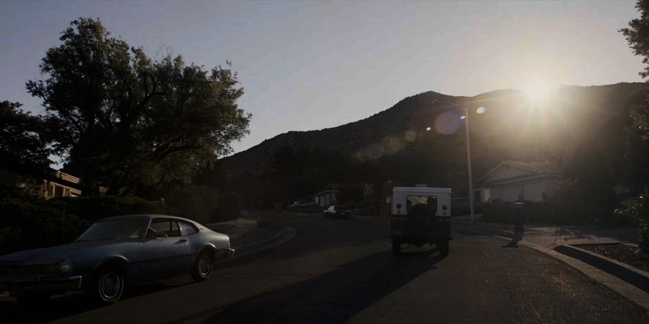 The mail carrier drives down the street as the sun crests the nearby hill.