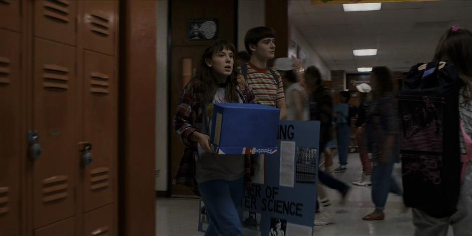 El and Will walk down the hallway with their presentation materials.