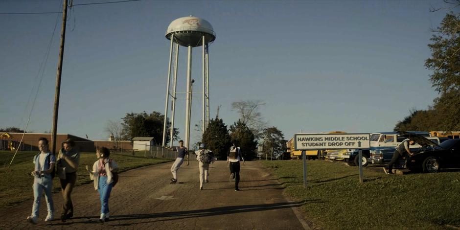 Dustin and Mike run up the drive towards the middle school to talk with Erica.