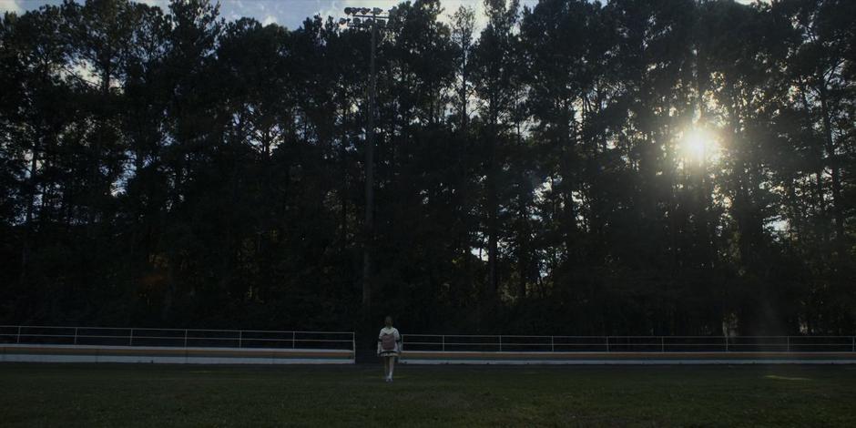 Chrissy crosses the field into the woods.