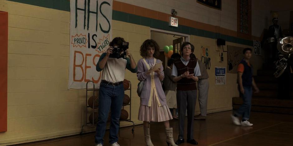 Nancy, Fred, and the newspaper's photographer watch the game from the sidelines.