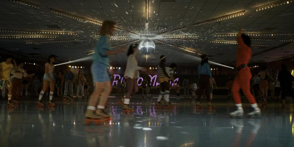 People skate around the rink with a disco ball shining from above.