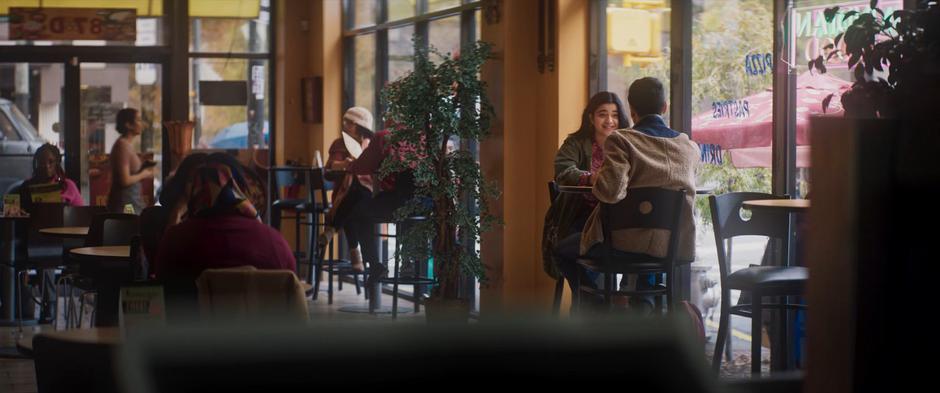 Kamala smiles while talking to Kamran at a small table by the window.