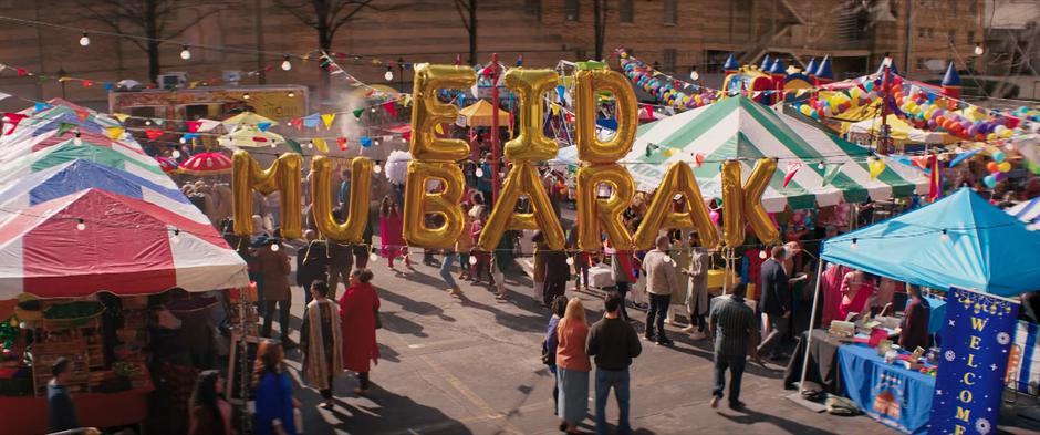 A balloon sign saying "Eid Mu Barak" hangs above the celebration in the lot behind the mosque.