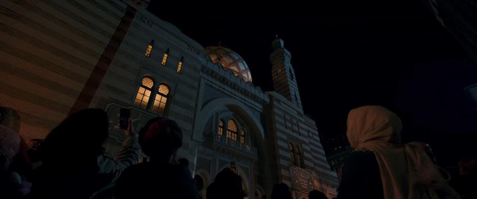 People watch from the ground as Kamala, in her costume, climbs around the outside of the roof to save the kid.