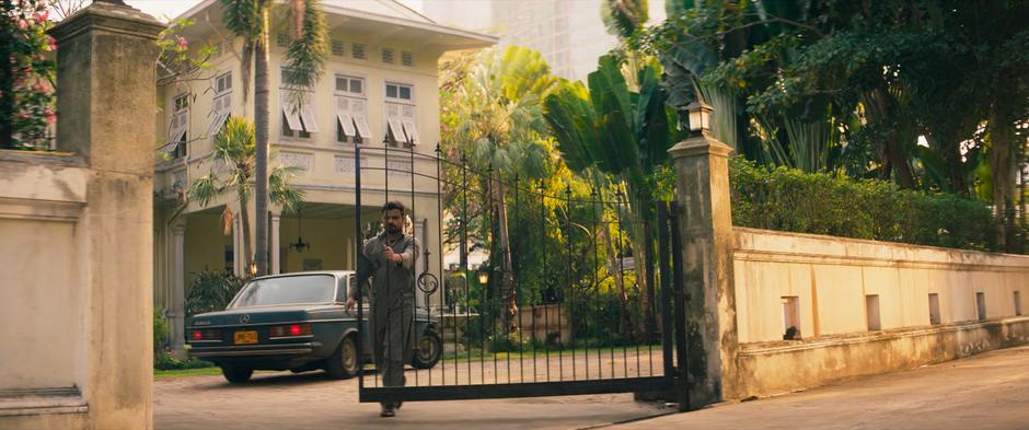 A man closes the gate as the car pulls to a stop in front of the house.