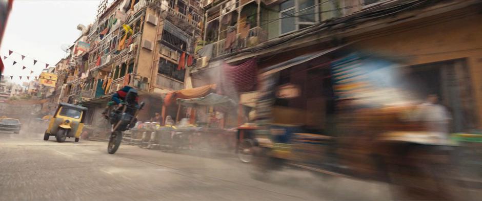 Kareem and Kamala balance on the single wheel of their motorcycle as they flee down the street.