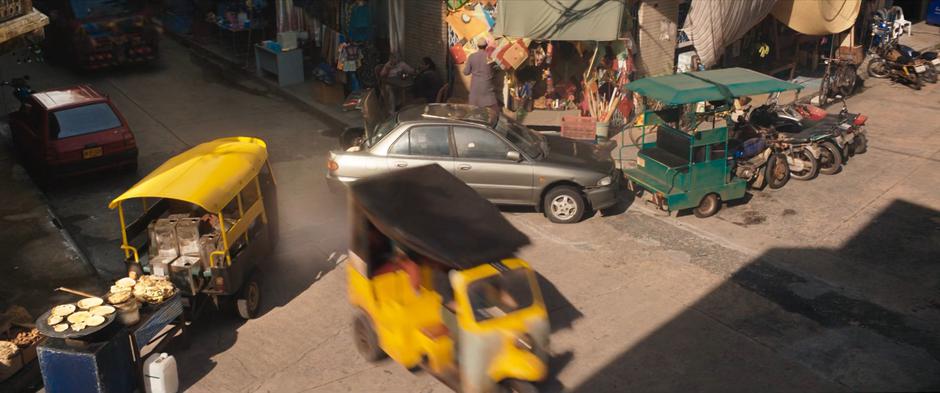 Kamala, Karren, and Waleed's stolen trike passes between two vehicles.