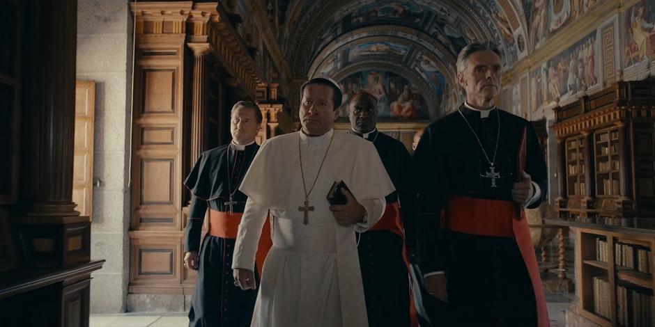 Pope Duretti, Cardinal Foster, and two more Cardinals walk through a lavishly decorated room.