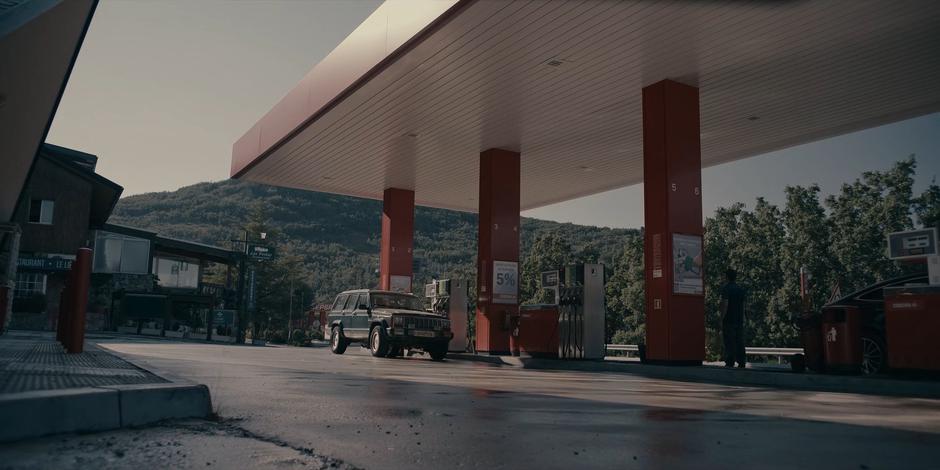 Miguel puts gas in the car while Ava and Bea sit inside.