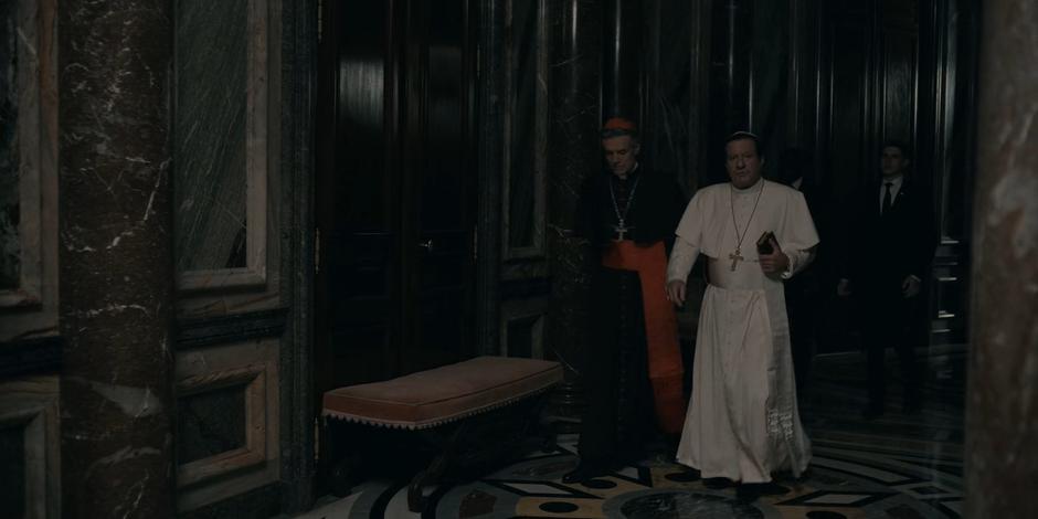 Cardinal Foster and Pope Duretti walk down the hallway.