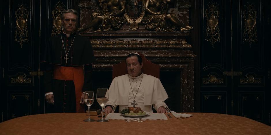 Cardinal Foster watches as Pope Duretti sits behind his meal.