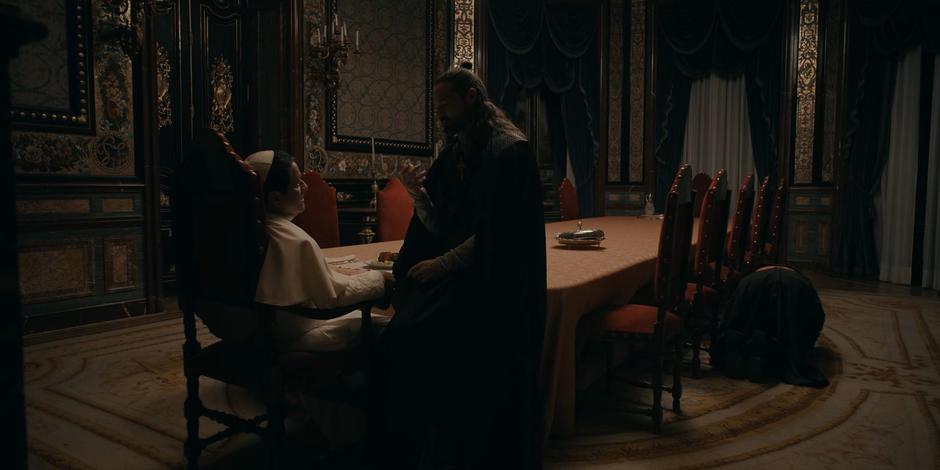 Adriel sits on the table in front of Pope Duretti while Cardinal Foster lies on the ground.