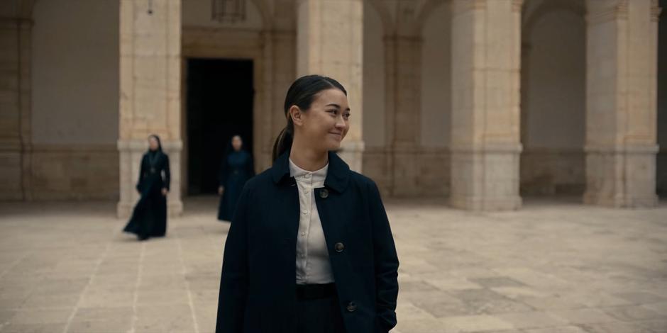 Bea smiles at the others as she crosses the courtyard.