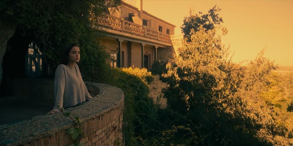 Ava stands on the balcony looking out over the landscape.