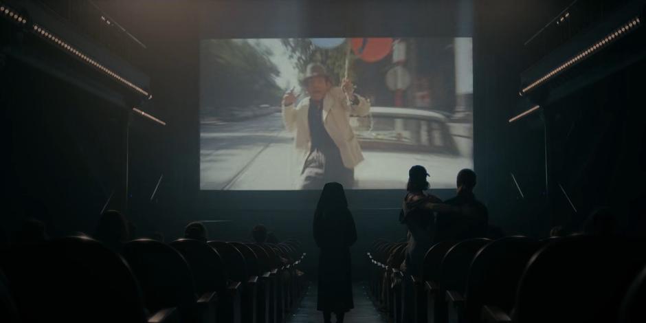 Camila stops while leading Ava and Bea through the cinema to watch a scene on the movie showing.