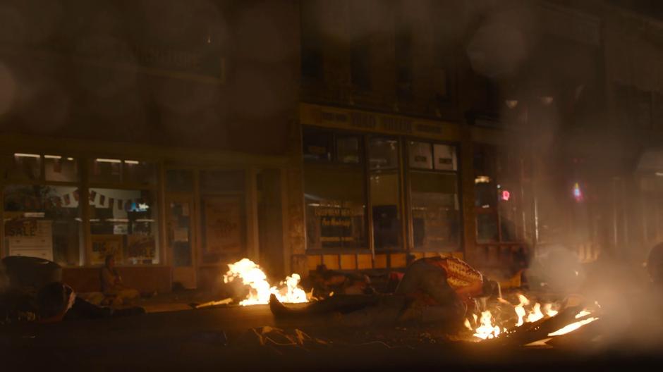 An infected chews on someone amongst the burning rubble in the street.