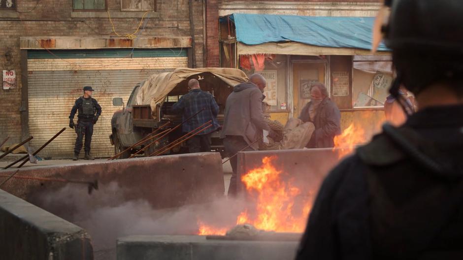 People take bodies from a truck and throw them into a bonfire.