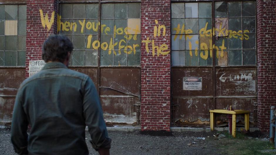 Joel steps away past some graffiti from the Fireflies.