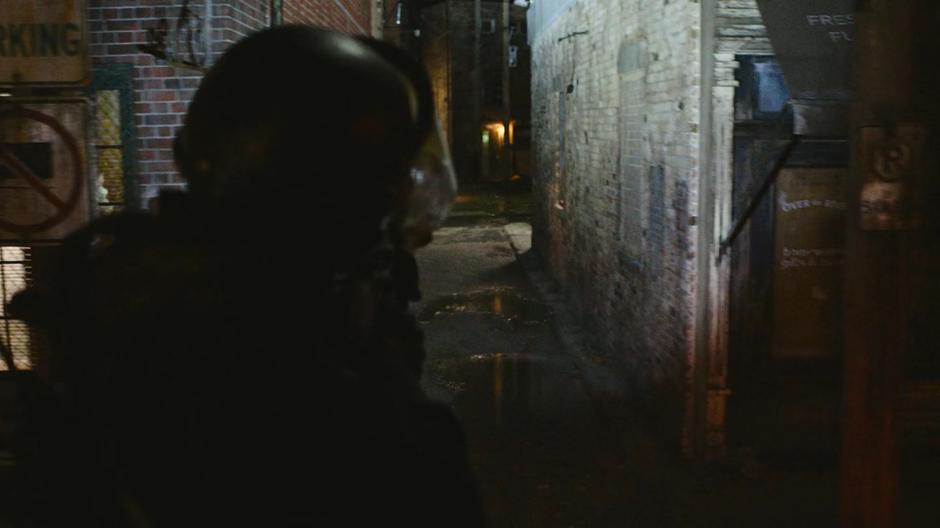 A FEDRA guard on a truck points their flashlight down a side alley at night.