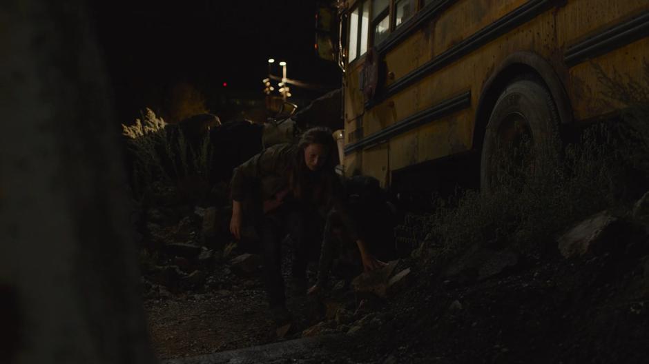 Tess and Ellie climb out from underneath a bus outside the wall.