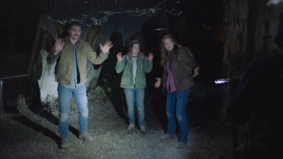 Joel, Ellie, and Tess put up their hands when Lee shines his flashlight on them.