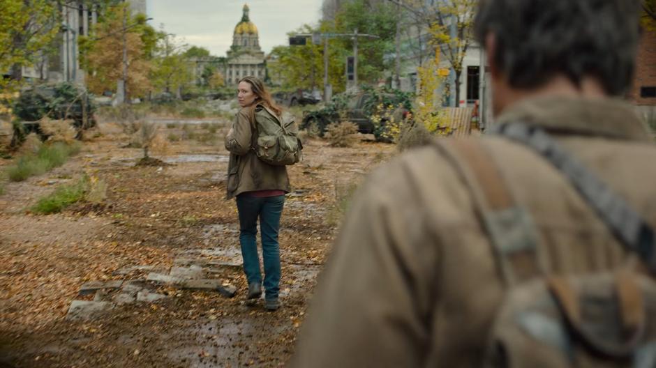 Tess glances over her shoulder at Joel as they walk towards the capitol.