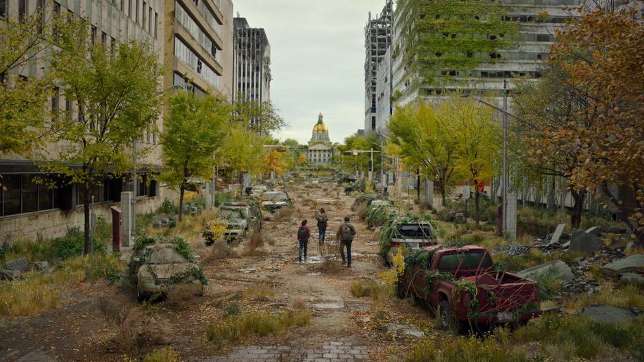 Ellie, Tess, and Joel walk down the overgrown street towards the capitol in the distance.