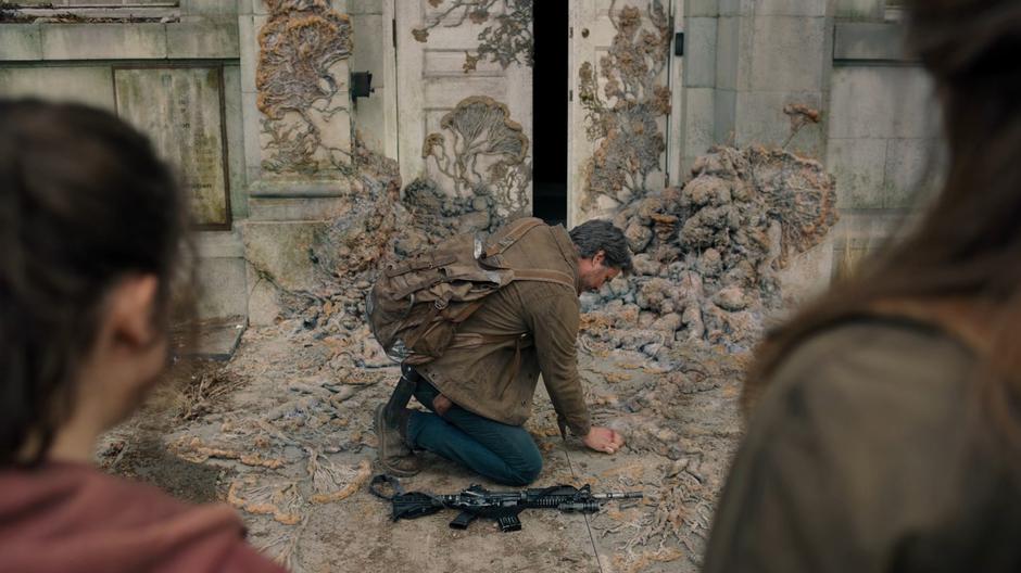 Joel kneels down to examine the tendrils while Ellie and Tess watch.