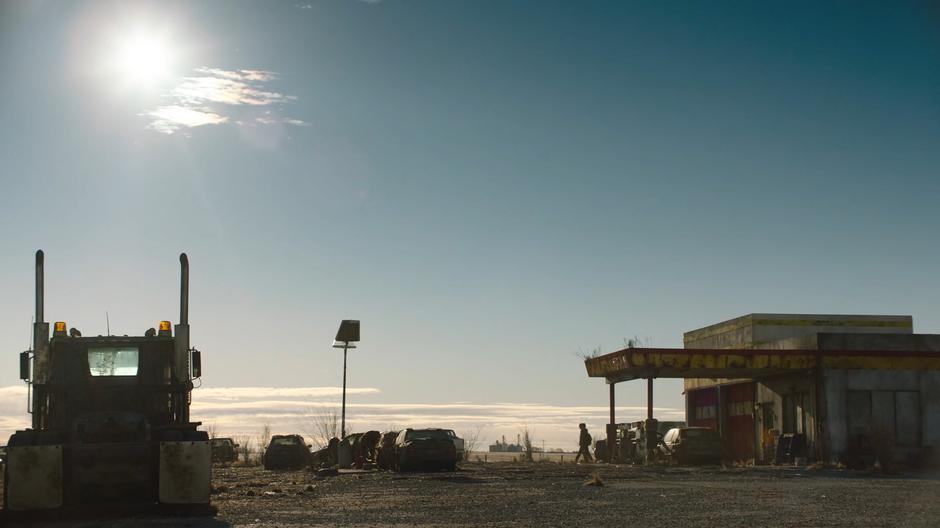 Ellie walks out of the service station to where Joel is siphoning gas.