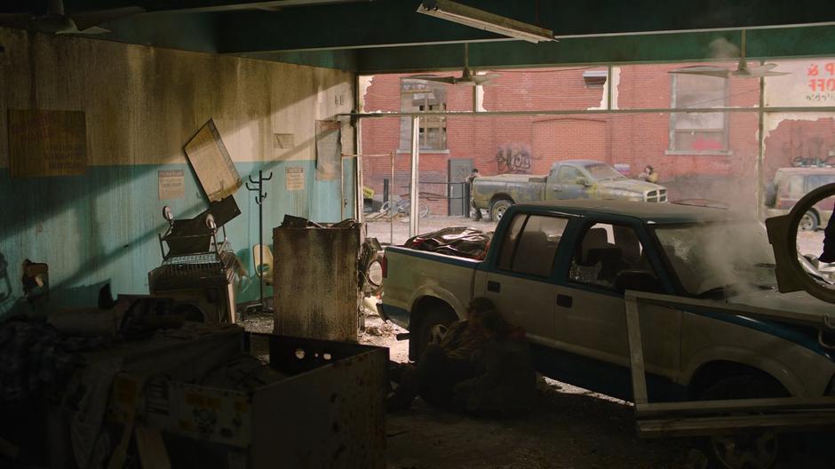 Joel and Ellie take shelter behind the car in the laundromat as two men fire at them from out in the alley.