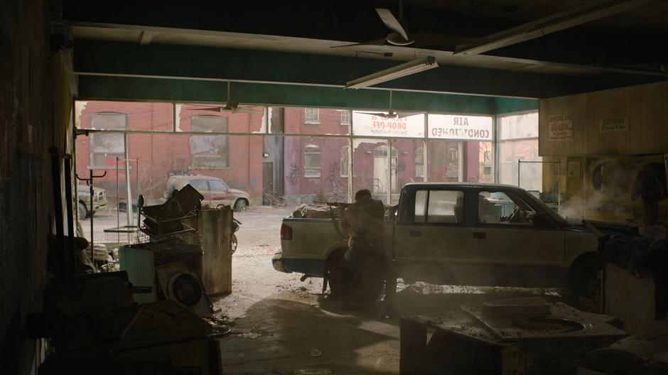 Joel fires at the guys on the street while Ellie clambers through the hole in the wall of the laundromat.