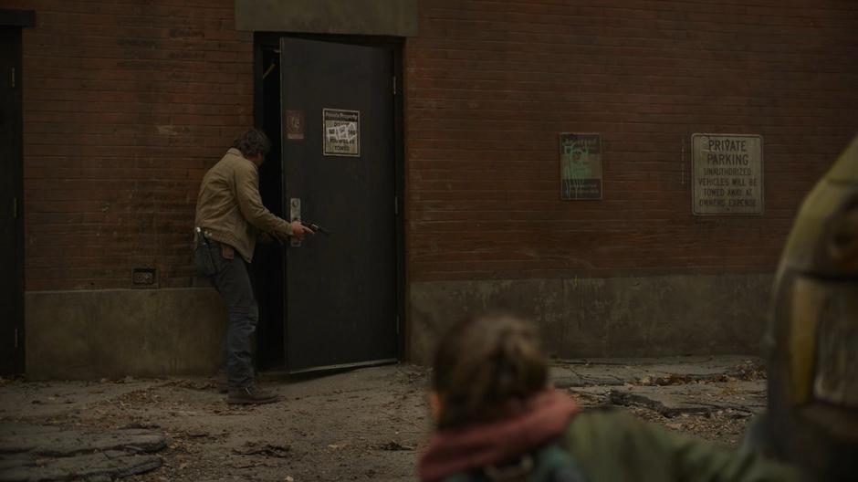 Joel checks a door across the alley while Ellie watches.