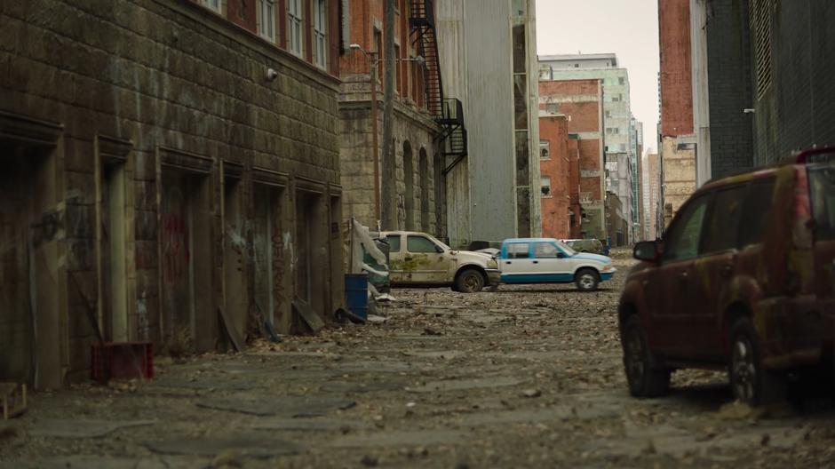 Joel and Ellie drive down the street past decrepit cars.