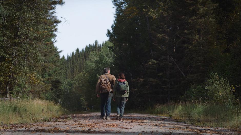 Joel leads Ellie down the road through the woods.