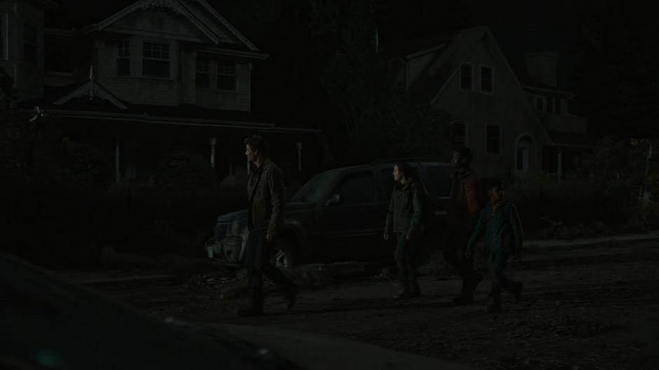 Joel looks around while leading Ellie, Henry, and Sam down the street.