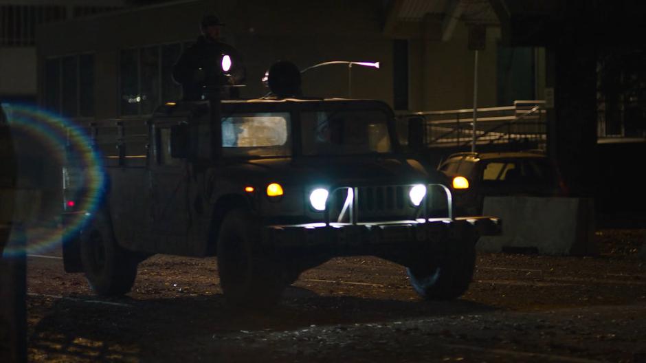 A humvee drives down the street with a revolutionary on top shines a search light around.