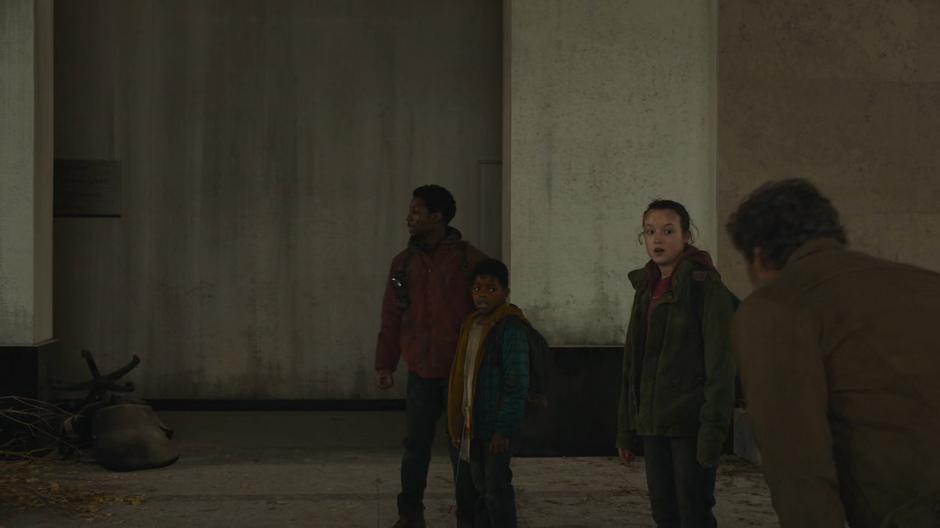 Sam and Ellie look over at Joel while Henry searches for the entrance to the tunnels.