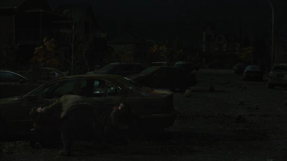 Joel pushes Henry, Sam, and Ellie into cover behind a car after they are attacked by a sniper.