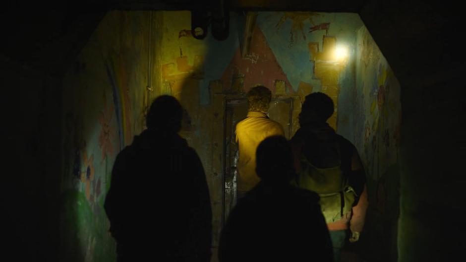 Ellie, Joel, Sam, and Henry emerge into a small chamber covered in artwork.