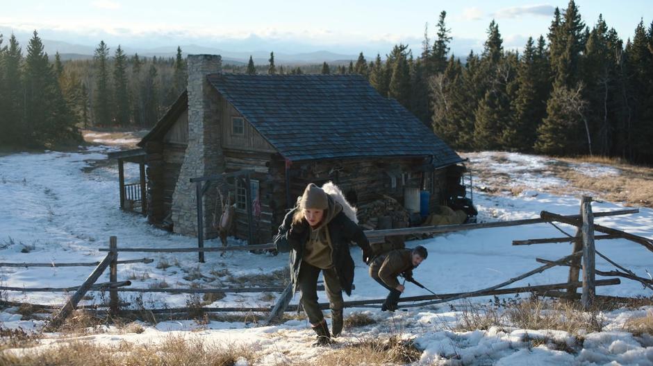 Joel ducks under the fence following Ellie as they leave the cabin.