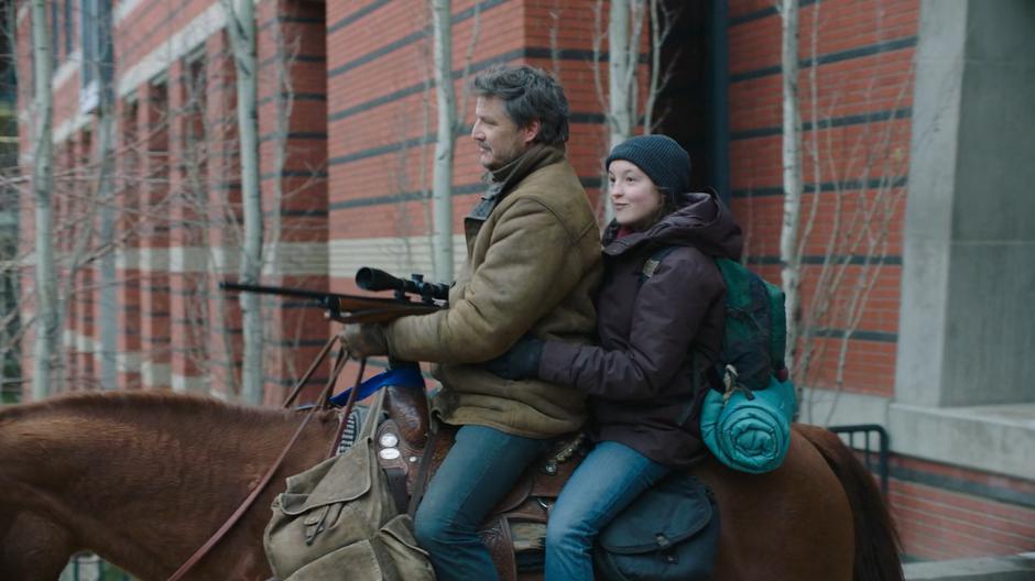 Ellie smiles as she and Joel ride out from between the two buildings.