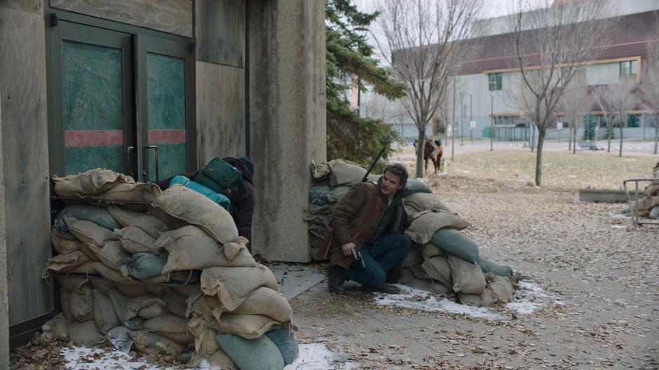 Ellie and Joel take cover behind some sandbags as they sneak out the back door of the lab.