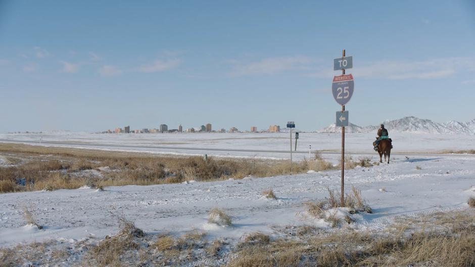 Joel and Ellie turn the corner at the sign for I-25 with the Boulder skyline in the distance.